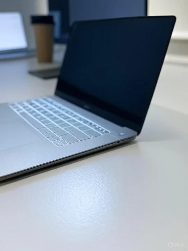 Sleek silver laptop on a white desk with a takeaway coffee cup in the blurred background.